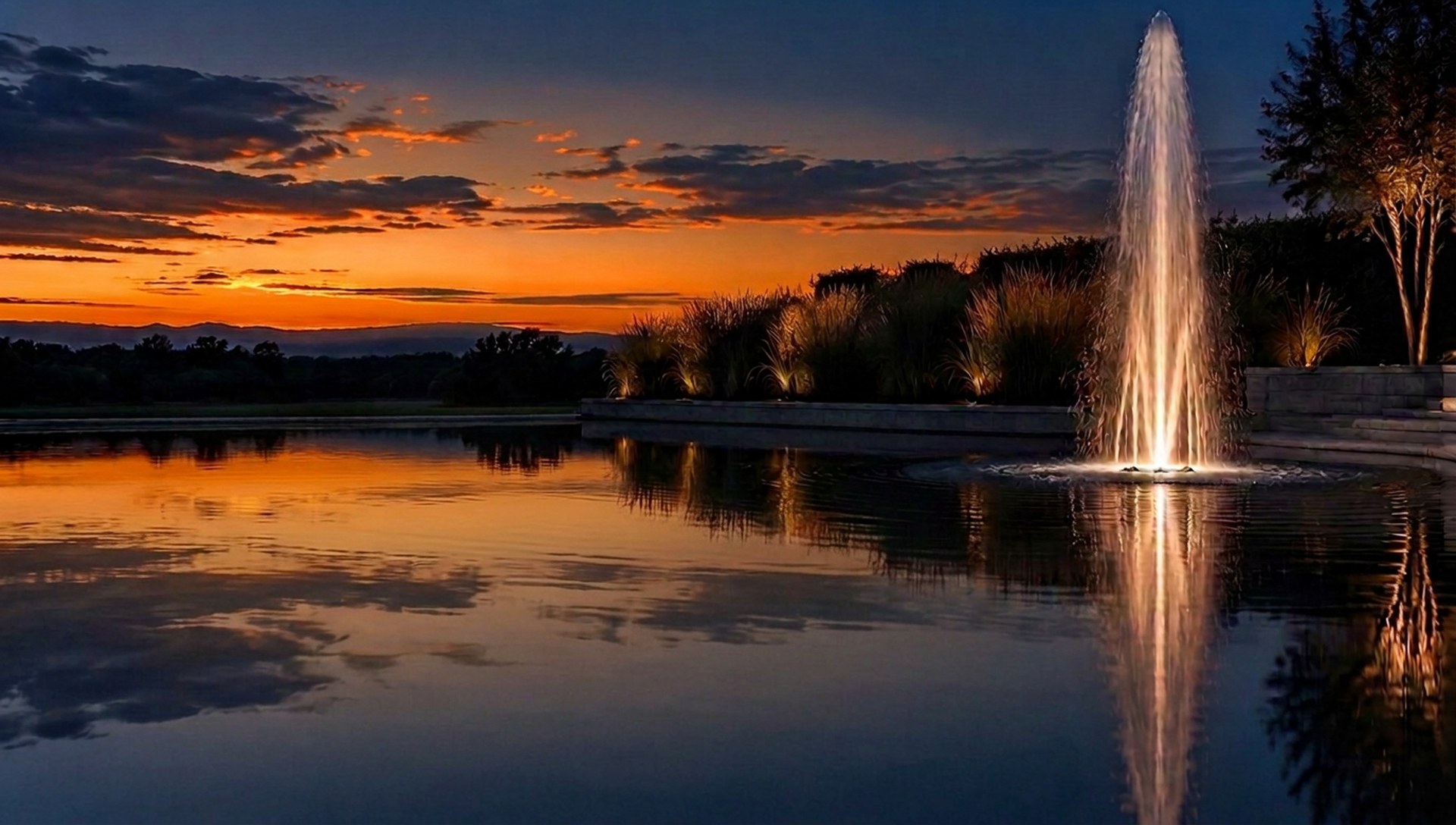 Garden pond with an illuminated fountain and a glowing sunset
